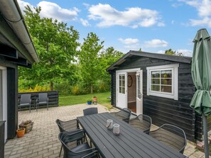Eine Holzhütte mit einer Terrassenfläche, Sitzgelegenheiten im Freien und einem grünen Sonnenschirm.