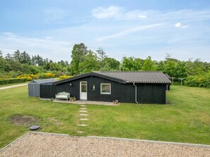 Ein eingeschossiges Gebäude mit Satteldach, einer kleinen Veranda und einem Weg zum Eingang.