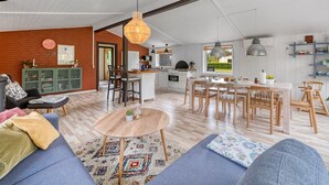A spacious living area with a sofa, coffee table, and dining table. There is a kitchen with a dining area, a brick wall, and a large window. - "Valdemar" - 350m to the fjord by Interhome (Tarm)