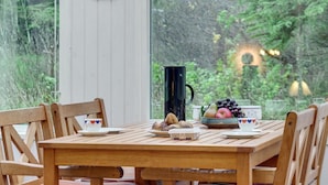 Een houten tafel gedekt voor een maaltijd, met uitzicht op groen en een gebouw op de achtergrond.