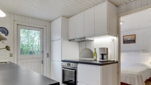Een compacte keuken met witte kastjes, een ingebouwde oven en een koffiezetapparaat op het aanrecht.