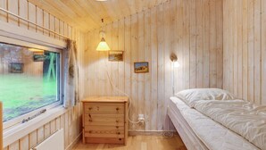 Een houten kamer met een bed, een houten dressoir, een raam en een wandlamp.
