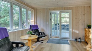 A room with a wooden ceiling, large windows, a sliding glass door, a black leather sofa, a small round table, and a wooden cabinet. - "Siljan" -  from the sea by Interhome (Hals)