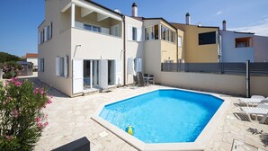 Ett tvåvåningshus med en swimmingpool, utemöbler och en trädgård.