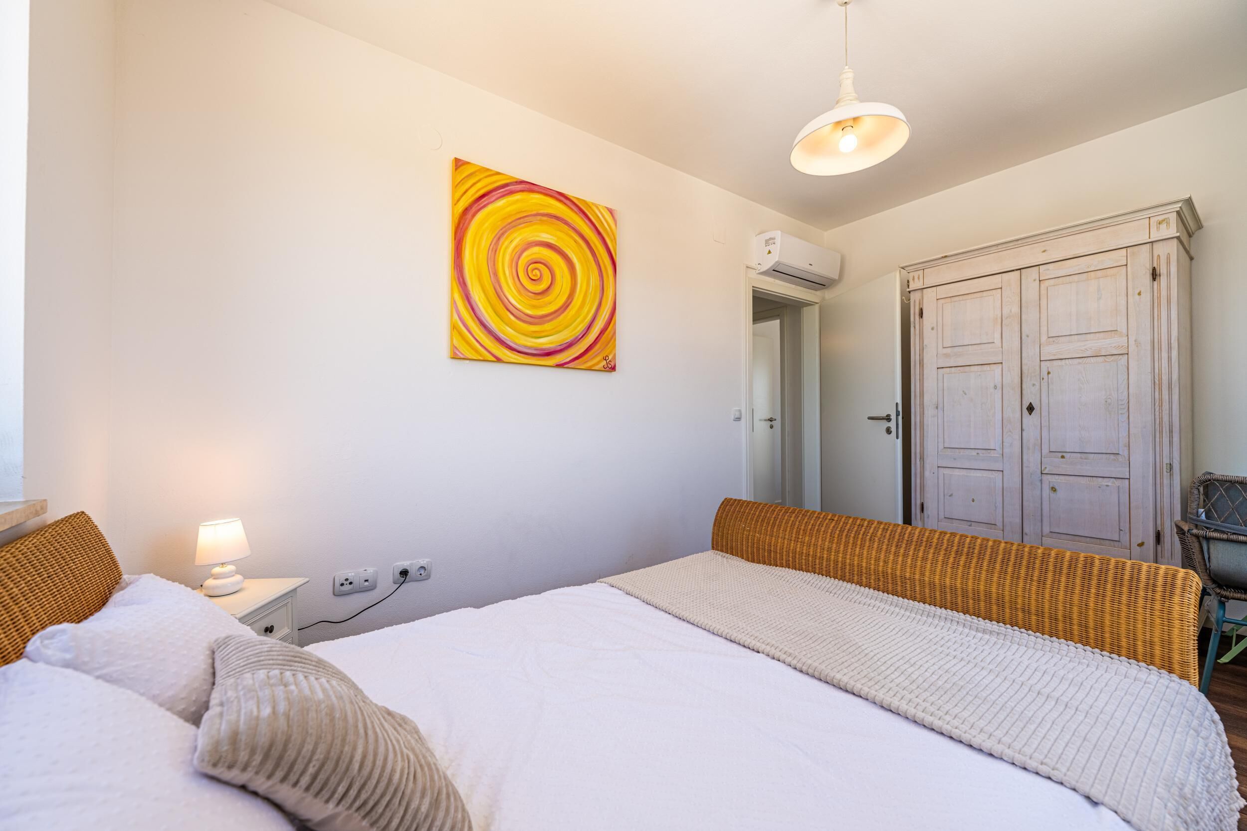 Et soveværelse med seng, natbord, lampe, garderobe og et maleri på væggen.
