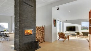A modern living room with a fireplace, wooden flooring, a dining area with chairs, a TV, and a bookshelf.