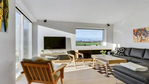 A modern living room with a large TV, a sofa, a dining table, and a view of the outdoors.