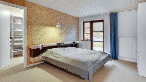 A bedroom with a bed, a wooden wall, a built-in shelf, a window, and a radiator.