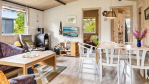 Een gezellige woonkamer met een open haard, een televisie en een eethoek met witte stoelen.