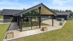 A modern house with a large glass patio, a wooden deck, and a covered outdoor seating area.