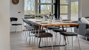 A modern dining area with a wooden table, black chairs, and large windows offering a view of trees.