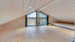 A spacious attic room with wooden slats on the ceiling and a large window.