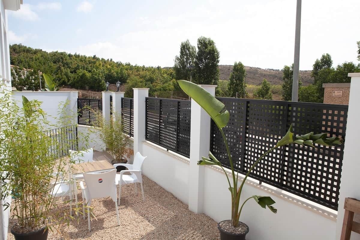 A patio with white chairs, a potted plant, and a black fence.