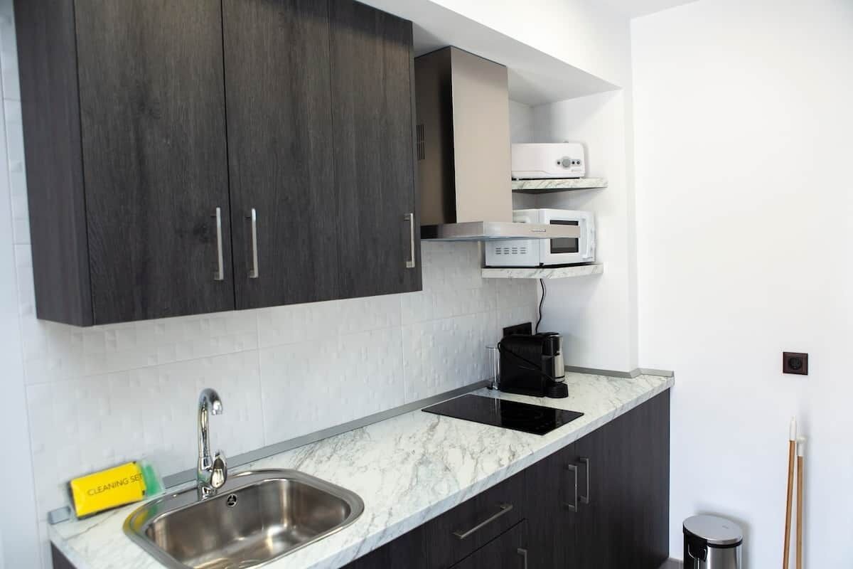 A modern kitchen with dark cabinets, a stainless steel sink, a microwave, and a coffee maker.