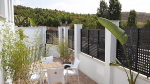 Une terrasse avec des chaises blanches et une table, entourée d’un mur blanc et d’une clôture noire.