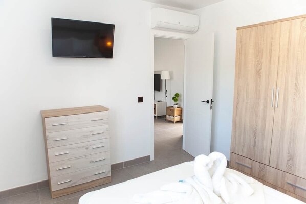A bedroom with a bed, a wooden dresser, a wardrobe, and a television on the wall.