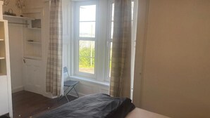A bedroom with a bed, a window with curtains, a chair, and a wardrobe. - Clydeview Apartments Langbank ( Gateway to Highlands ) (Langbank)