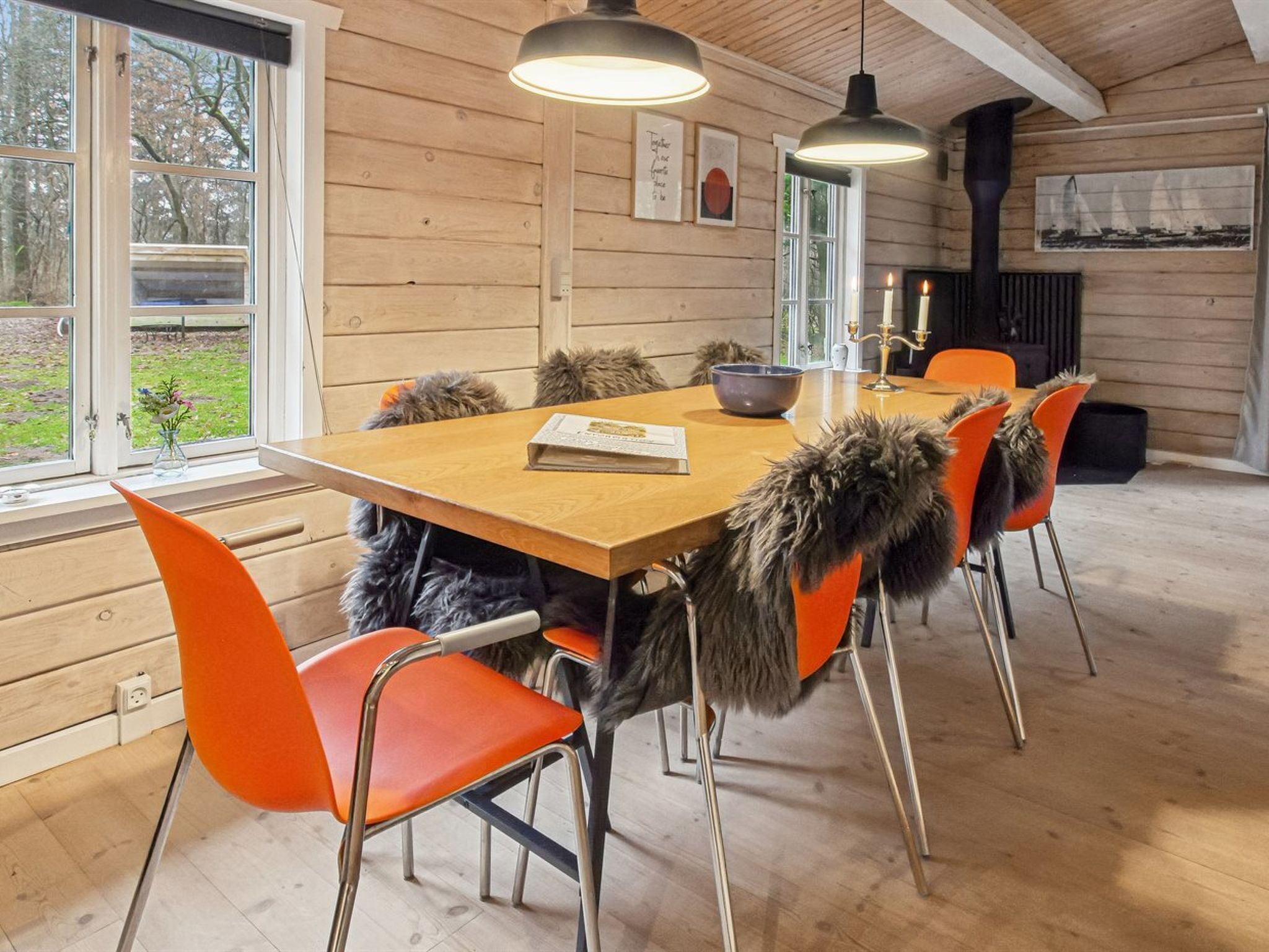 A wooden interior with a dining table, orange chairs, and a fireplace.