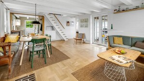 Un vaste espace de vie agrémenté d’un escalier en bois, d’une table à manger avec des chaises, d’un canapé et d’une table basse sur laquelle se trouve un saladier rempli de fruits.