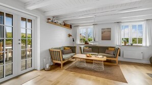 Un salon spacieux doté d’un plancher en bois, d’un ensemble de canapés, d’une table basse et offrant une vue sur l’extérieur grâce à de grandes fenêtres.