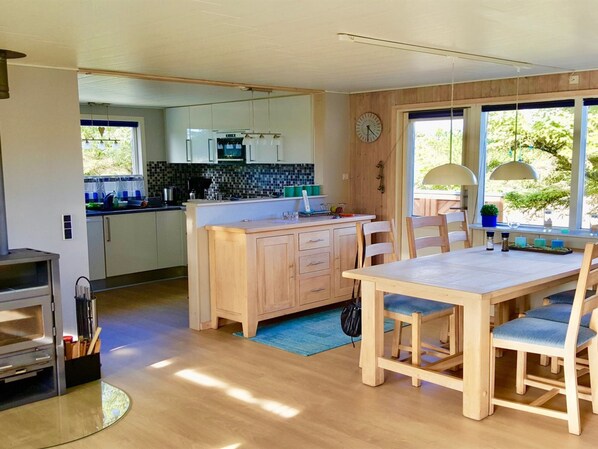 A modern kitchen with wooden cabinets, a central island, and a dining area with a table and chairs.