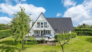Een wit huis met twee verdiepingen, een betegeld dak, een balkon met stoelen en een verzorgd gazon.