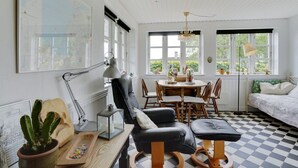 Een kamer met een zwart-wit geruit vloertje, een zwarte leren bank, een houten eettafel met stoelen, en een bed met een wit en groen geboeide spreidekking.