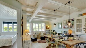 Een ruime kamer met een groot bed, een eethoek met houten meubels, en een keuken met witte kasten en een hanglamp.