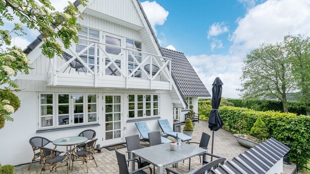 Een wit huis met een ruim terras, buitenmeubels en een overdekt gedeelte.