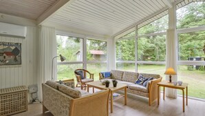 A spacious room with a high ceiling, large windows offering a view of the outdoors, a sofa, chairs, a table, and a lamp. - "Chrissie" - 150m from the sea by Interhome (Hals)