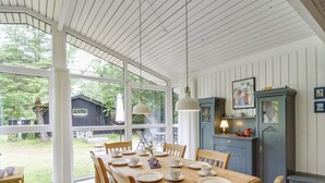 A dining area with a wooden table set for four, surrounded by chairs. There is a blue cabinet with a lamp on top, and a small table with a bench to the side. - "Chrissie" - 150m from the sea by Interhome (Hals)