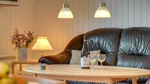 Un salon chaleureux avec un canapé en cuir, une table basse ronde en bois, une bouteille de vin et deux verres à vin.
