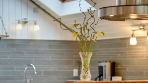 Une cuisine moderne avec un vase en verre transparent posé sur le comptoir, une hotte de cuisine en acier inoxydable et un dosseret de carrelage gris.