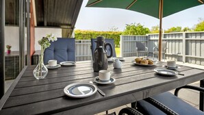 Une table dressée à l’extérieur, avec un parasol vert, un vase rempli de fleurs et une assiette de muffins.