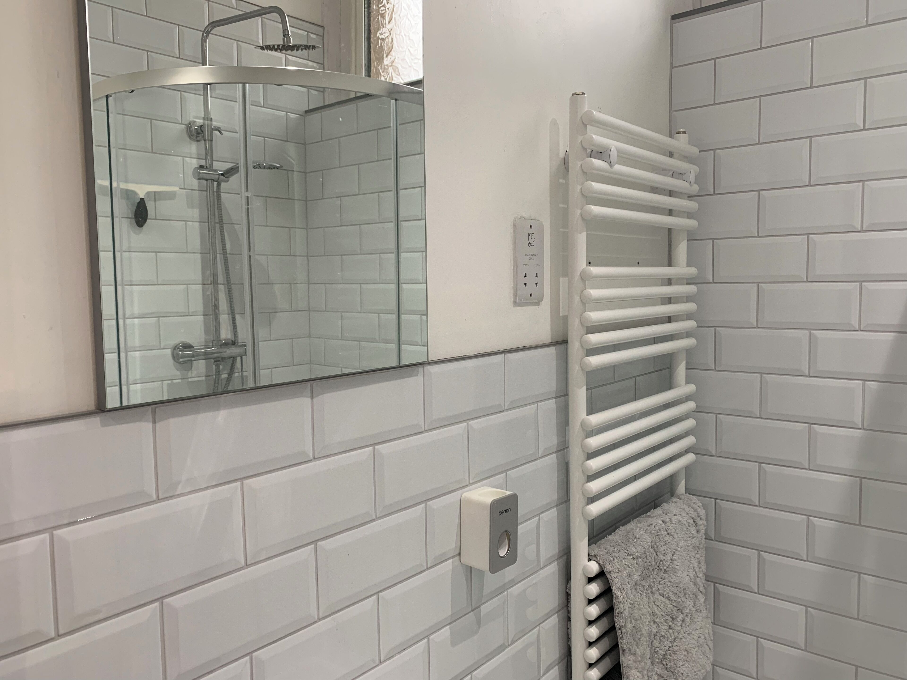 A bathroom with a glass-enclosed shower, a white towel rack, and a white tiled wall.
