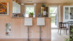 Een moderne keuken met houten kasten, twee witte barkrukken, een centraal eiland en een eethoek met een tafel en stoelen.