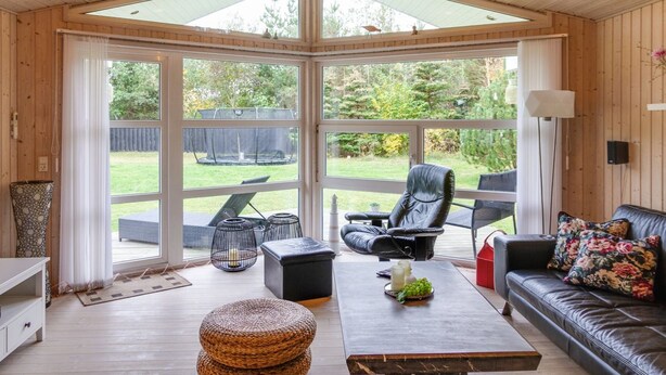 Een gezellige kamer met houten plafond, grote ramen, een leren bank, een bijzettafeltje en uitzicht op de tuin.