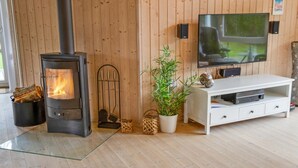 Een woonkamer met een houtkachel, een televisie en een witte tv-meubel.