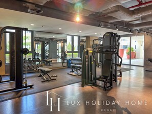 A spacious gym with various exercise equipment, large windows, and a polished floor.