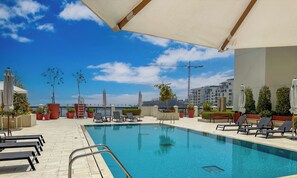 Un área de piscina en la azotea con sillones de descanso, plantas en macetas y una vista despejada del horizonte urbano.