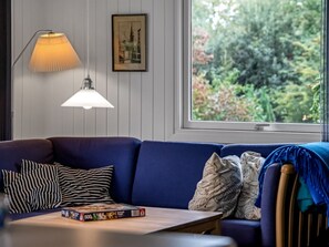 Une pièce avec un canapé bleu, des coussins à rayures, une table sur laquelle est posé un jeu de société, une lampe et un tableau encadré au mur.