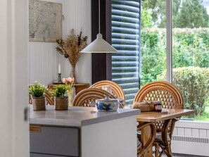 Un comedor con una mesa dispuesta para dos personas, con sillas de mimbre, un jarrón con flores secas y un hervidor de té.