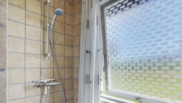 Une salle de bain avec une douche, des murs carrelés et une fenêtre donnant sur un mur extérieur orné de motifs.