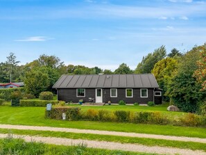 Een laag gebouw met een donkere gevel, een plat dak en een klein voortuintje met een stoel.