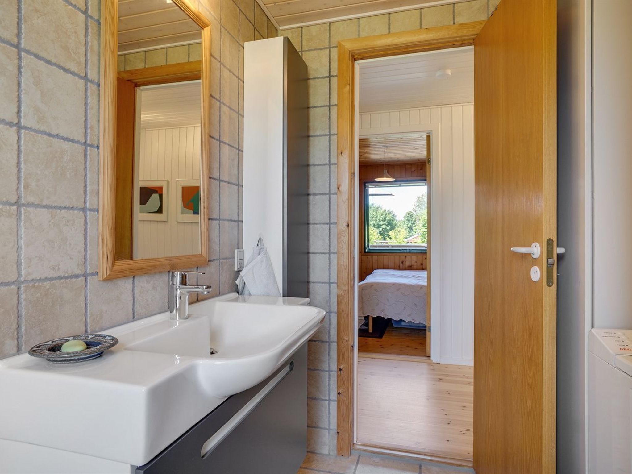 Een moderne badkamer met een grote wastafel, een spiegel en een houten deur die naar een slaapkamer leidt.
