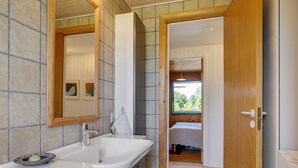 Une salle de bain moderne avec un grand lavabo, un miroir et une porte en bois donnant sur une chambre.