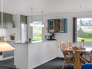 Une cuisine moderne avec des meubles blancs, un îlot central et un coin repas doté de chaises en osier.