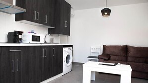 Une cuisine moderne avec des meubles de couleur sombre, un lave-linge, un four à micro-ondes et une table blanche.