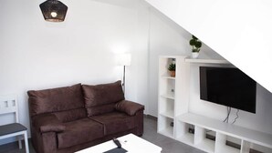 Un salon moderne avec un canapé marron, une table basse blanche, un téléviseur posé sur un meuble blanc, une lampe et une petite plante.