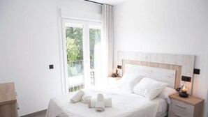 Une chambre d’hôtel avec un grand lit, une table de chevet avec une lampe, une tête de lit en bois et une vue sur la verdure par la fenêtre.